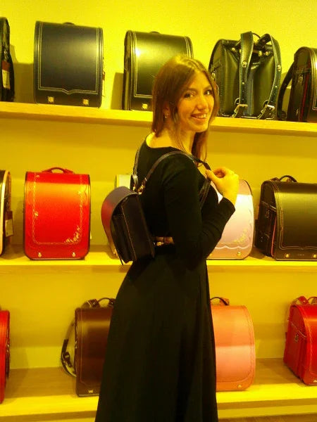 Woman wearing a Japanese randoseru backpack in a store with colorful backpacks on shelves