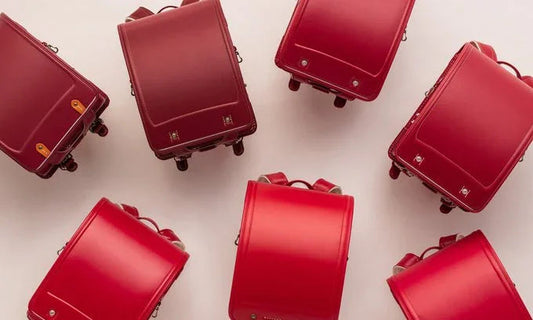 Seven red Japanese randoseru backpacks arranged on a light background, top view.