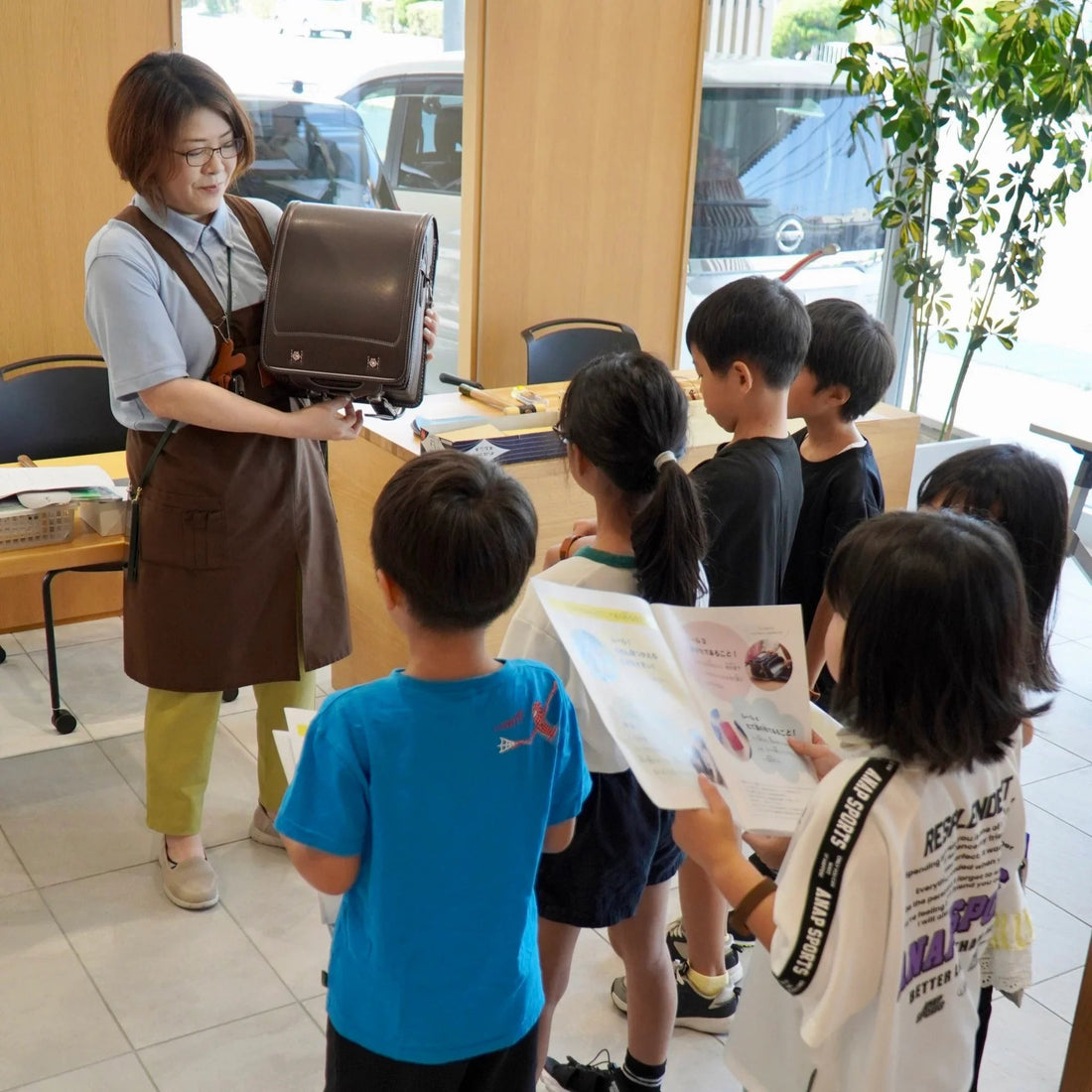 Woman showing Japanese randoseru backpack to group of children in a classroom setting