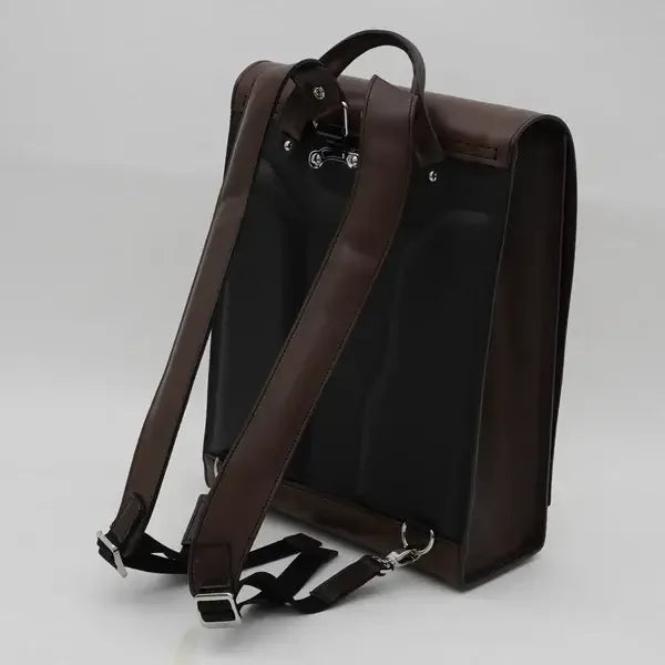 Black and brown Japanese randoseru backpack with adjustable straps on plain background