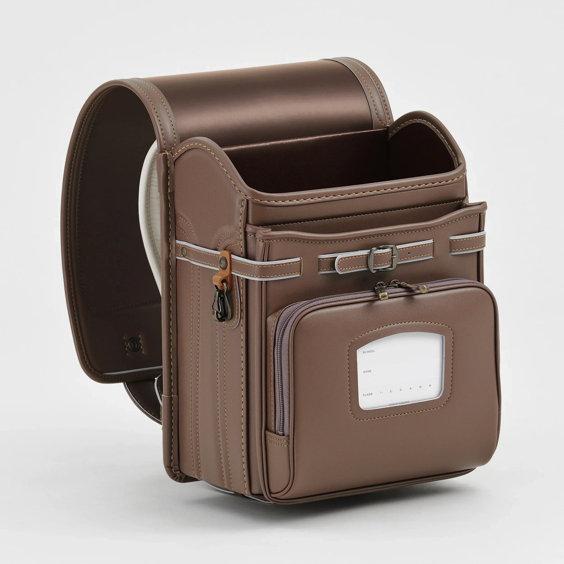 Brown Japanese randoseru backpack with front pocket and white label, studio background