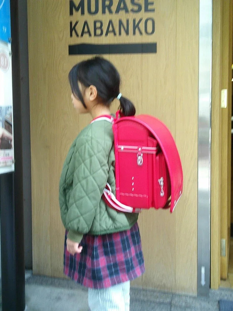 Girl wearing a red Japanese Randoseru backpack outside a store, side profile view