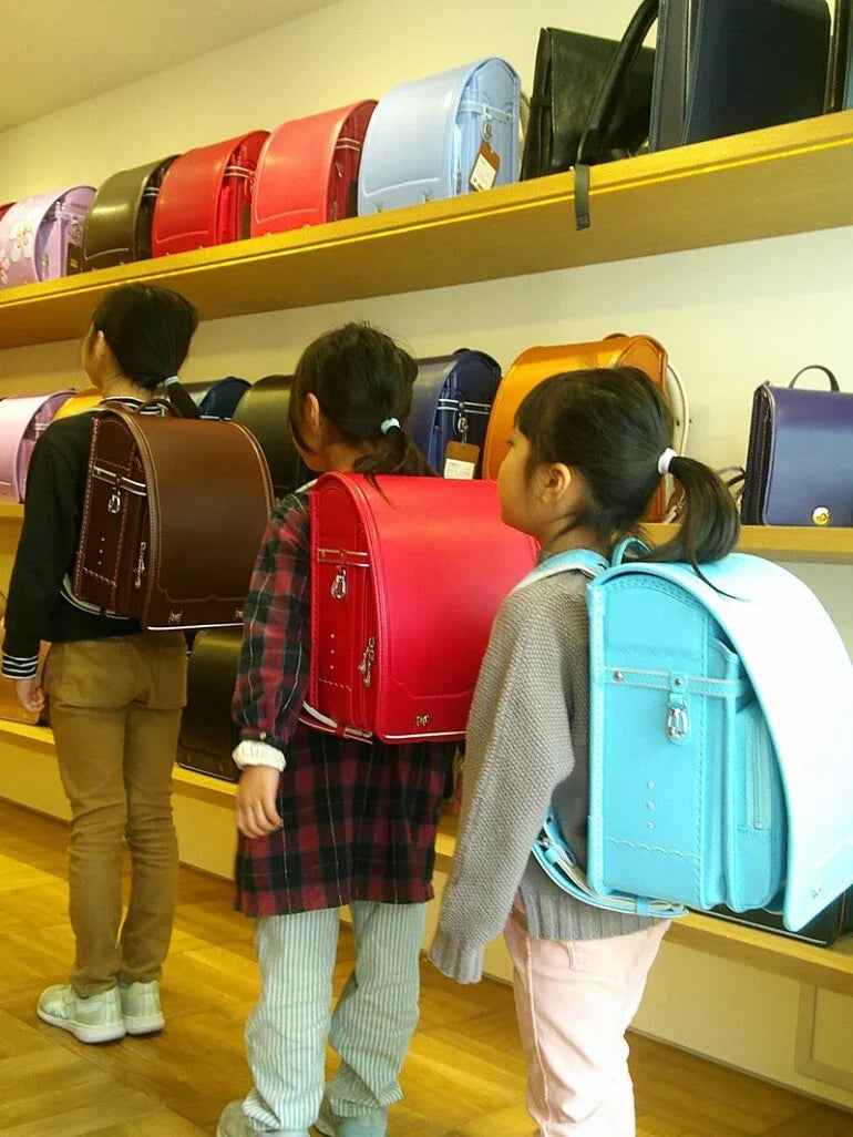 Children wearing Japanese randoseru backpacks in a shop with colorful backpacks on display shelves