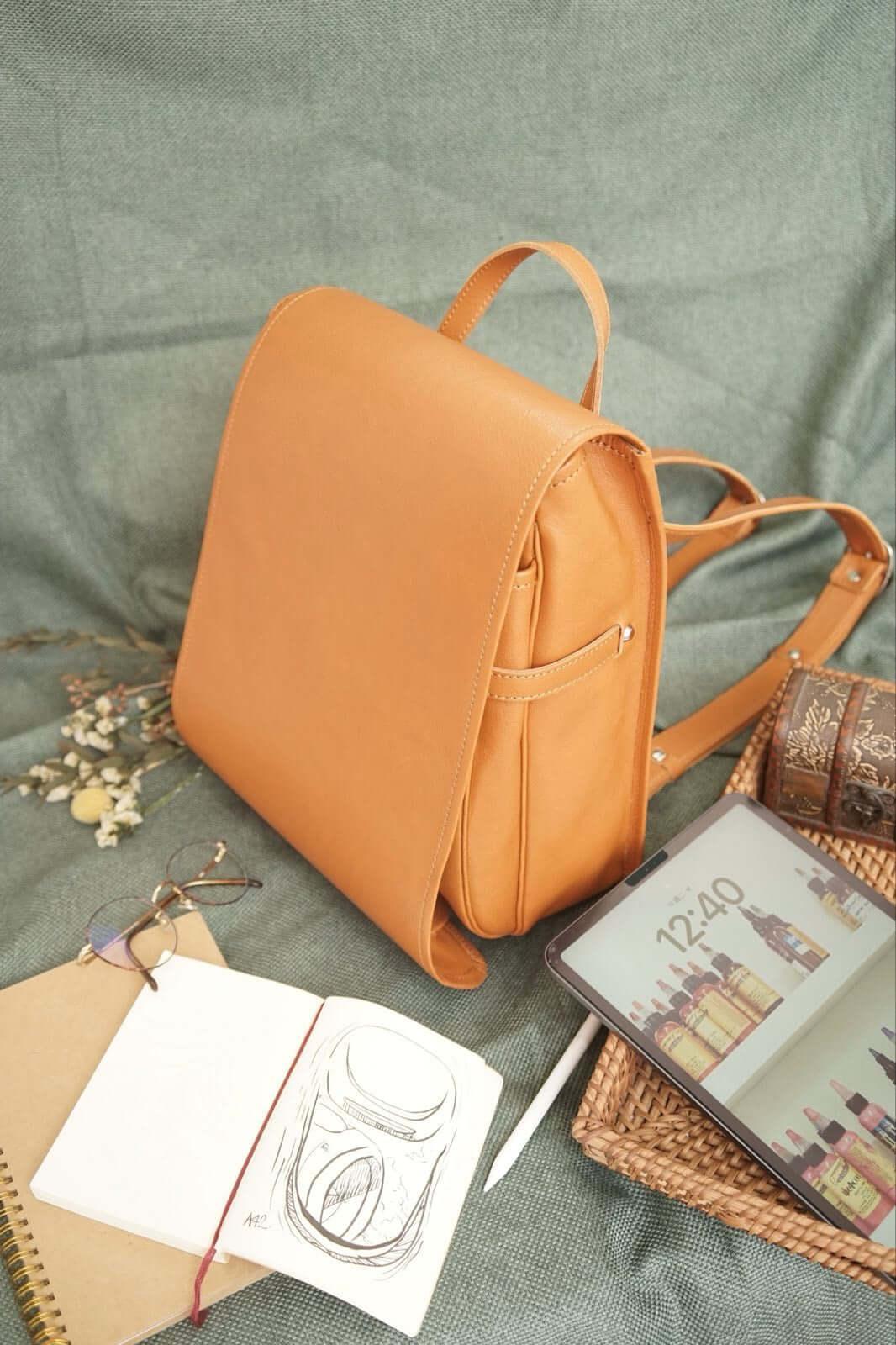 Murase Kabanko adults ransel backpack in camel leather with top handle and dual straps placed with notebook and tablet.